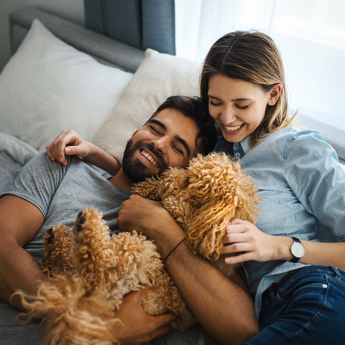 A happy couple cuddling on the couch with their little dog